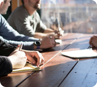 Imagen de personas sentadas en una mesa tomando nota y escuchando